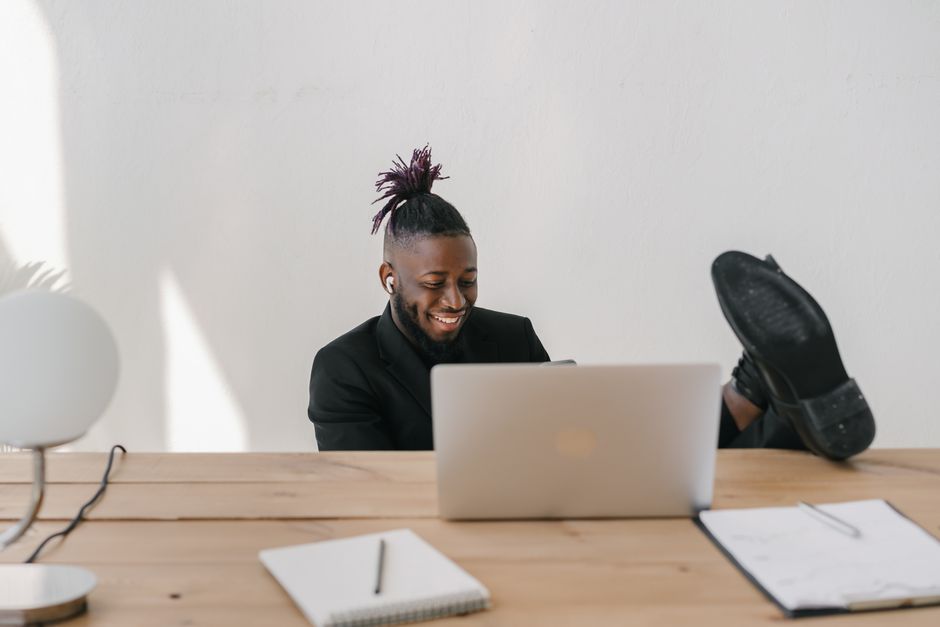Retenção de Talentos — Young man in a suit relaxing at a desk with a laptop, smiling.