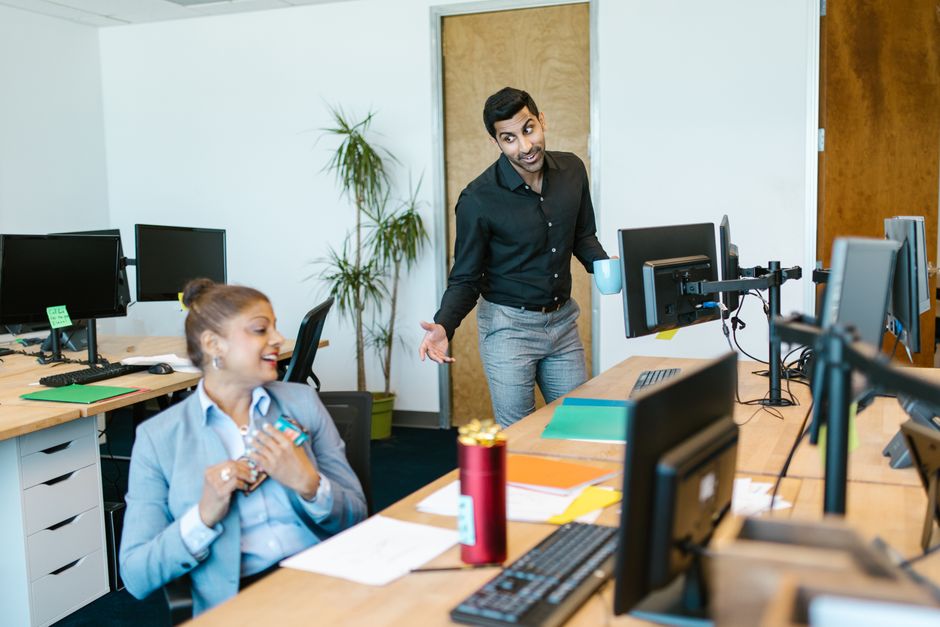 Retenção de Talentos — Two colleagues engaging in a cheerful conversation in a modern office setting.