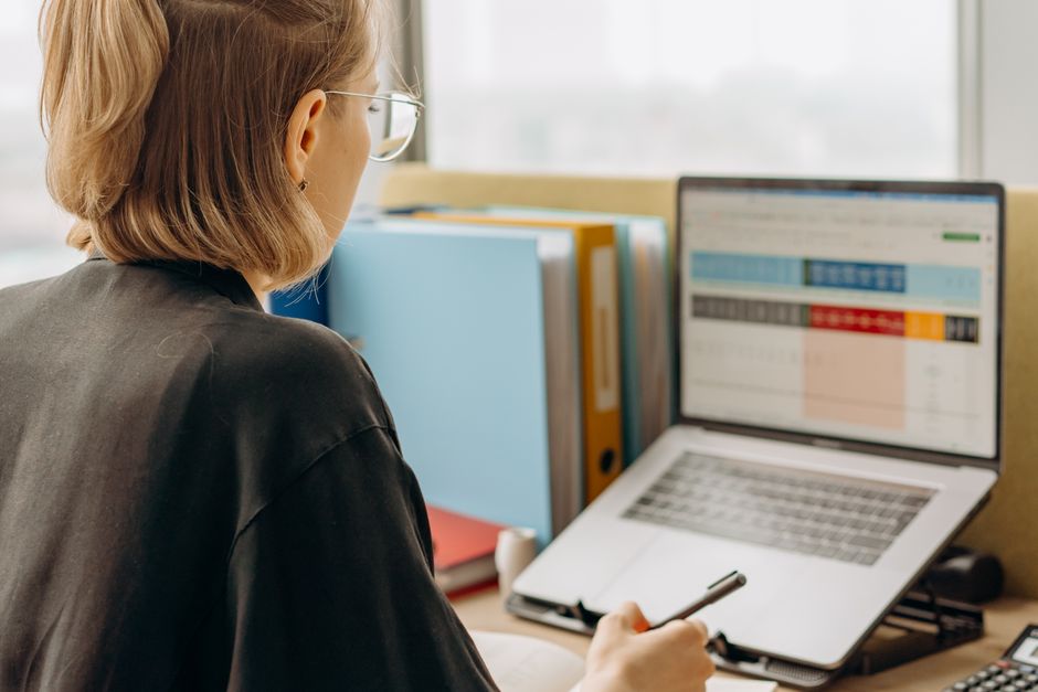 Retenção de Talentos — Professional woman reviewing data on laptop, working in modern office environment.
